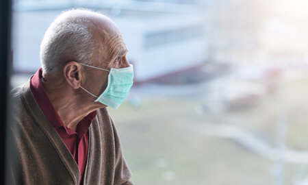 Spendenkampagne Vergissmeinnicht 2020: Ein älterer Herr mit Mundschutz blickt aus einem Fenster.