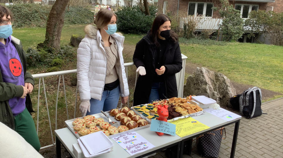 Ein Schüler und zwei Schülerinnen des Berufskolleg Michaelshoven stehen hinter einem Biertisch mit Essen. 