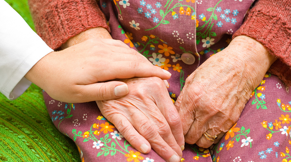 Altenpfleger/-in hält Hand von Seniorin