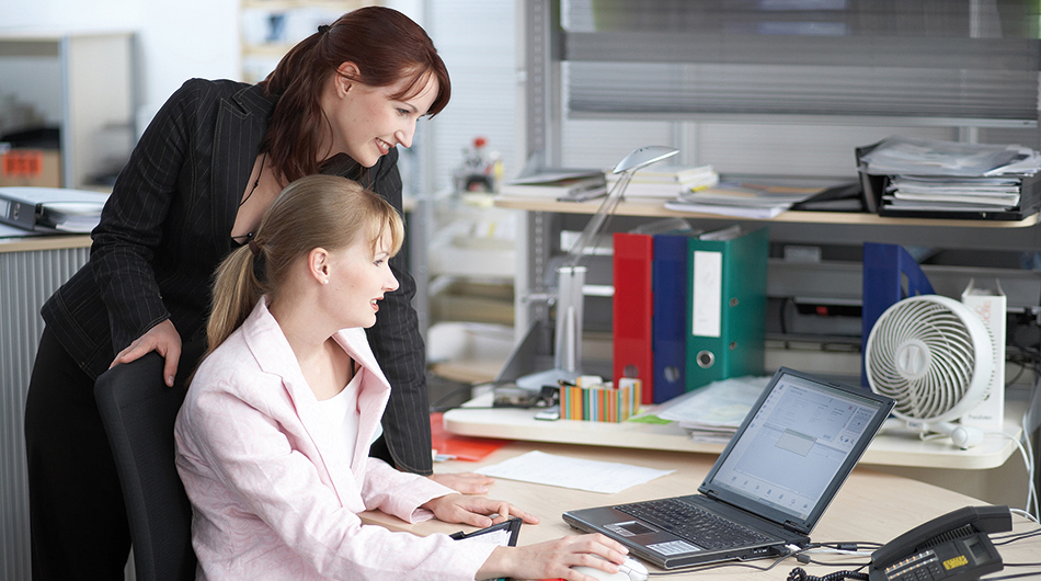 2 Frauen in der Ausbildung zum Kaufmann/zur Kauffrau für Büromanagement (Kölner Bildungsmodell) vor einem PC.