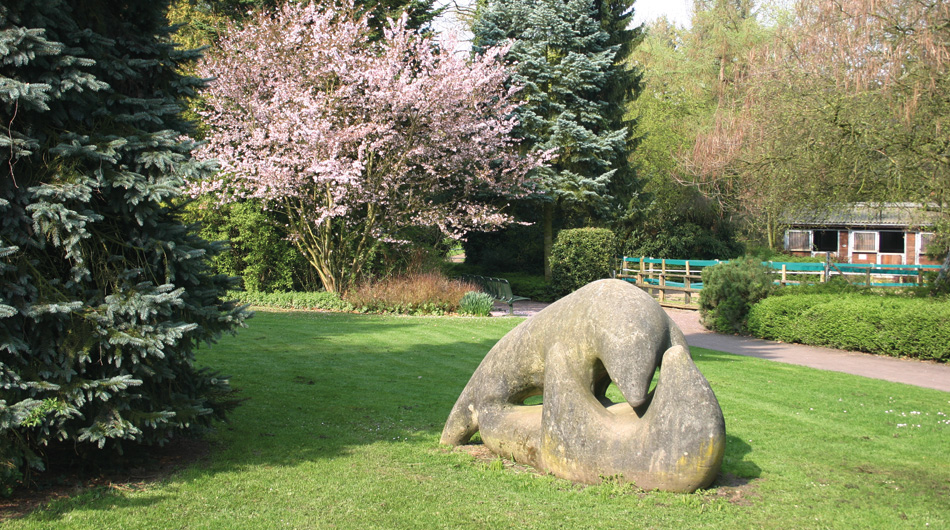 Eine Grünfläche mit Pflanzen, Bäumen und einer Skulptur im Park von Michaelshoven